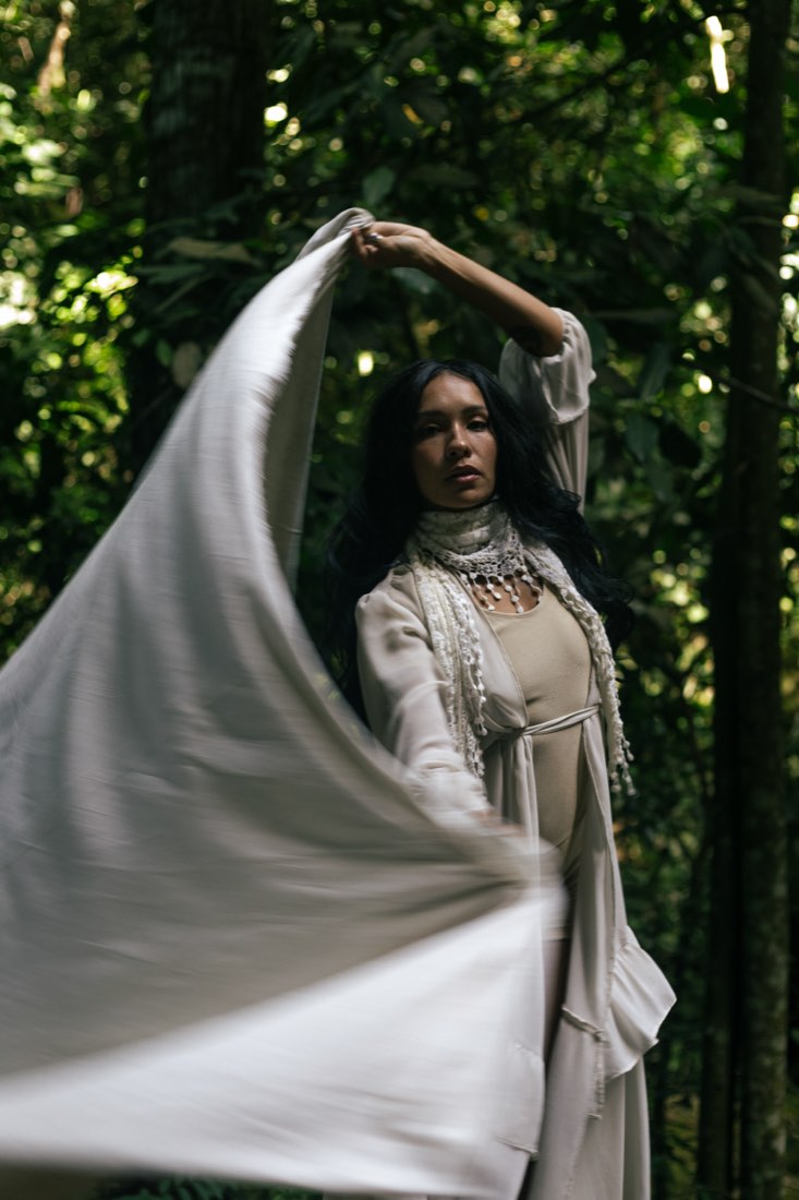 Figura vestida de branco entre os troncos das árvores.